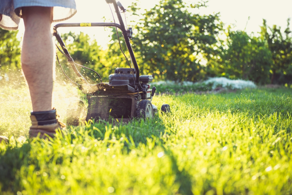 Boots and legs guiding a lawn mower through sunlit grass, capturing a calm start to a first time tax return UK for someone self employed after retirement.