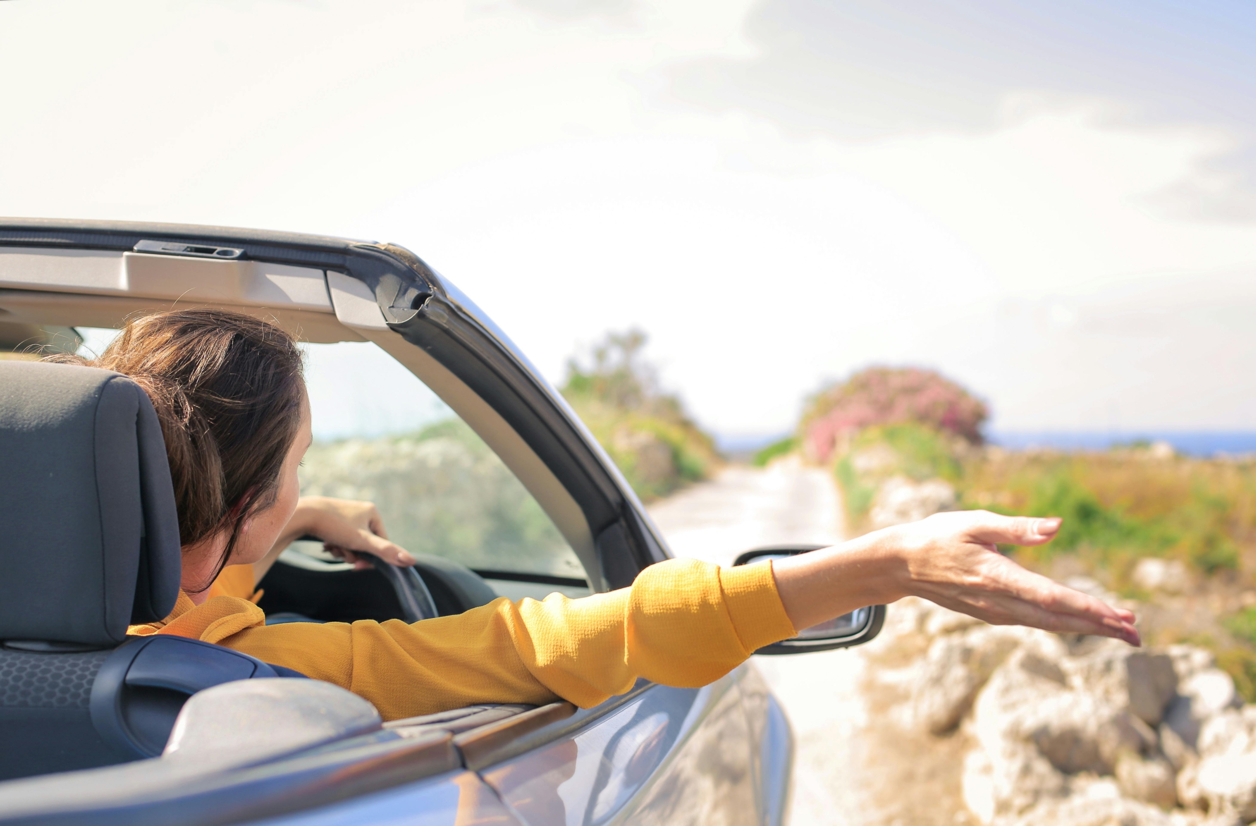 Female contractor driving with hand out of car window, symbolising freedom after closing a limited company and switching to self-assessment in the UK